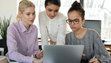 Focused multiracial female employees work on laptop together